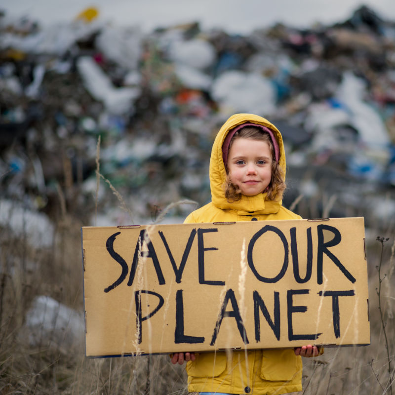 Front view of small child holding placard poster on landfill, environmental pollution concept.